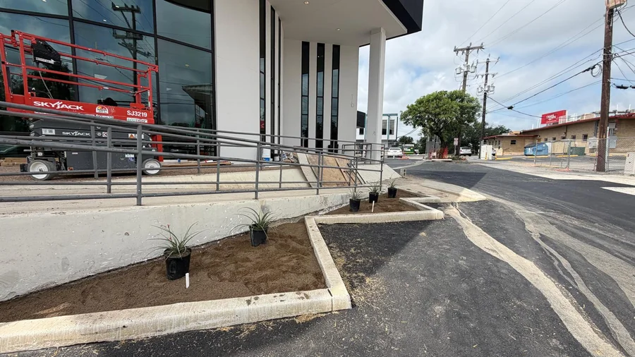 Curb and walkway transition beside a planted bed at a San Antonio building, a common commercial property trip hazard location